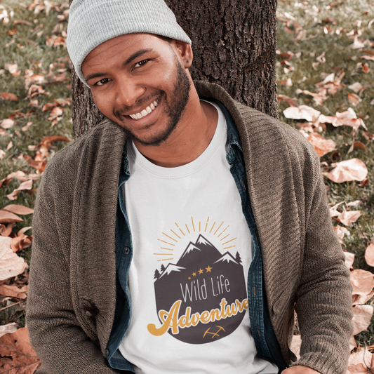 Man sitting on the ground with an open book, wearing a t-shirt with 'Wild Life Adventure' design.