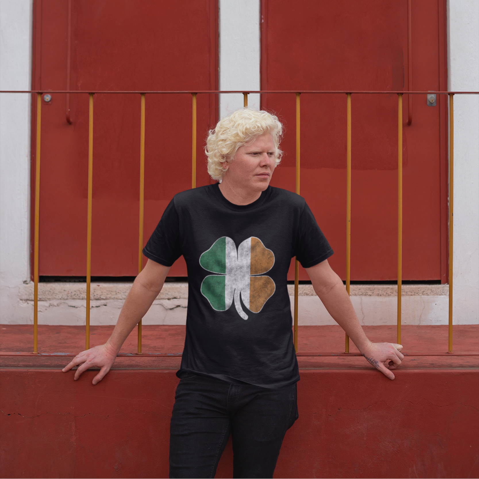 Person wearing a black t-shirt with a four-leaf clover design in front of red doors.