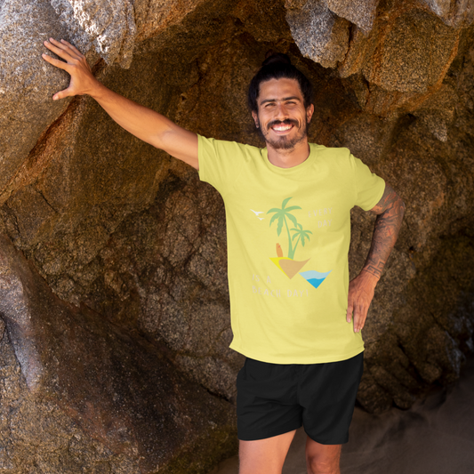 Man wearing a yellow t-shirt with a palm tree design, standing in a rocky cave on a beach.