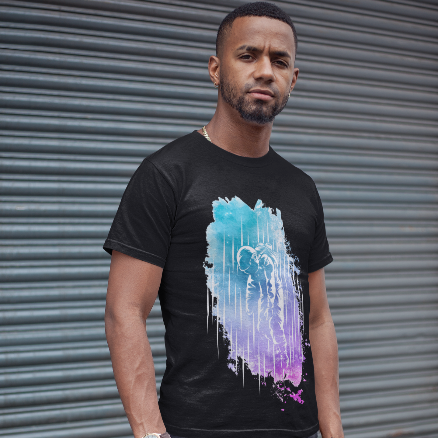 Man wearing a black t-shirt with a colorful abstract design in front of a gray metal shutter.