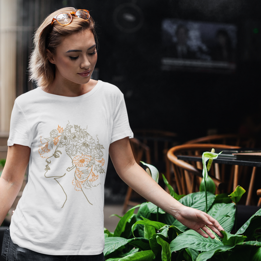 Woman wearing a white t-shirt with a graphic design, standing outdoors near green plants.