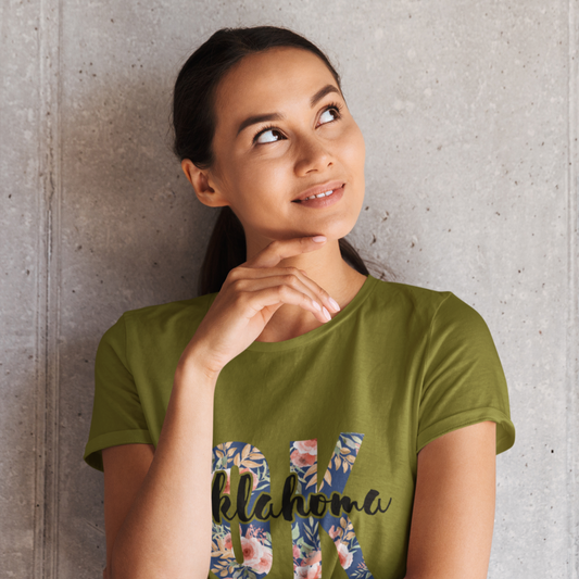 Woman wearing a green t-shirt with 'OKLAHOMA' design against a concrete wall.