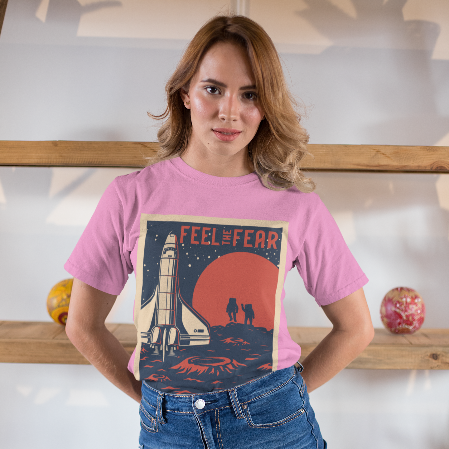 Woman wearing a pink t-shirt with a graphic design and text, standing indoors.