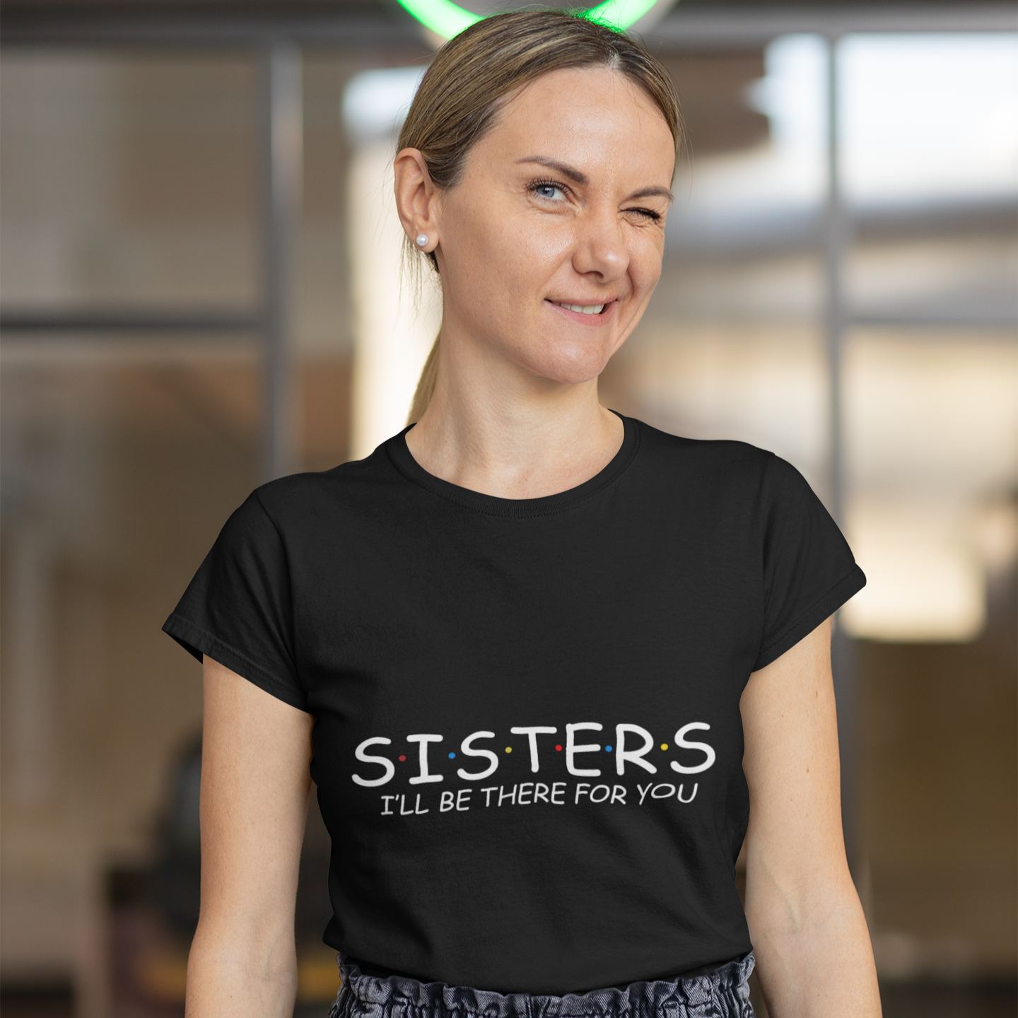 Woman wearing a black t-shirt with 'SISTERS I'll be there for you' text in an indoor setting.