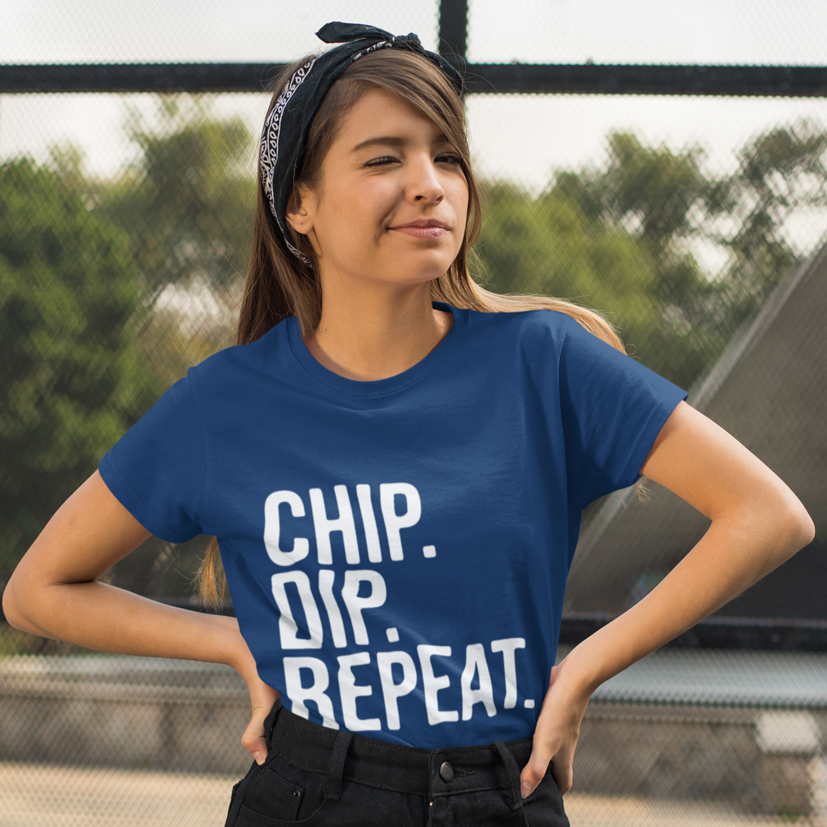 Woman wearing a blue t-shirt with 'CHIP. DIP. REPEAT' text, standing outdoors.