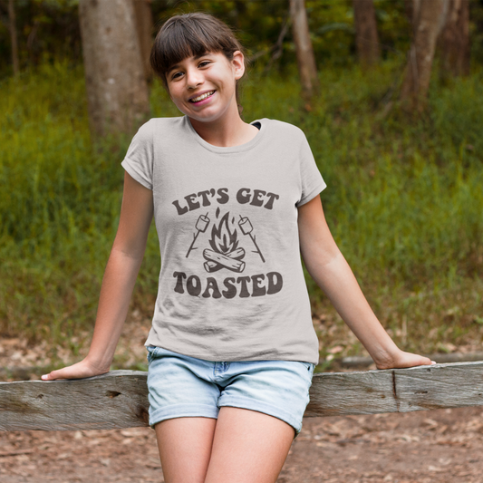 Child wearing a t-shirt with 'Let's Get Toasted' graphic in a forest setting