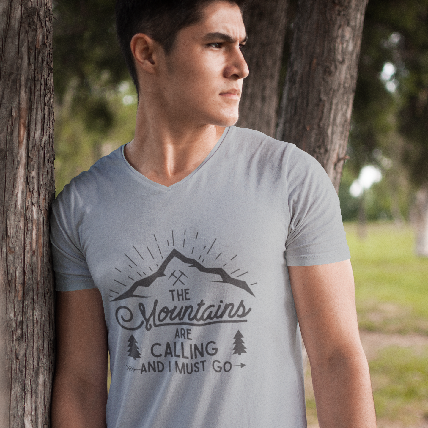 Man wearing a t-shirt with 'The Mountains Are Calling' text in a natural setting