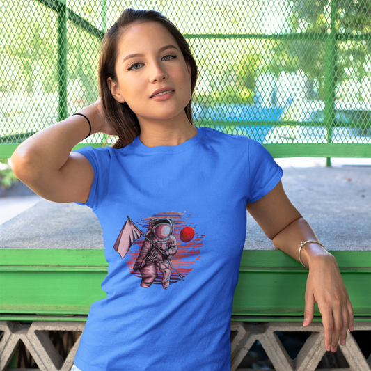 Woman wearing a blue t-shirt with a graphic design, standing against a green metal fence.