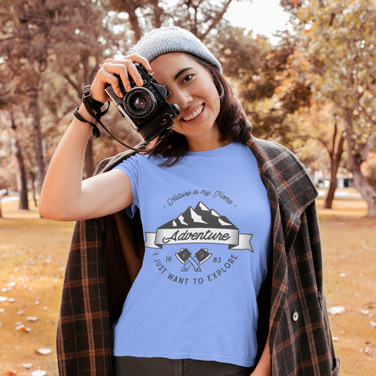 Person wearing a blue t-shirt with a mountain design and text, holding a camera in an outdoor setting.