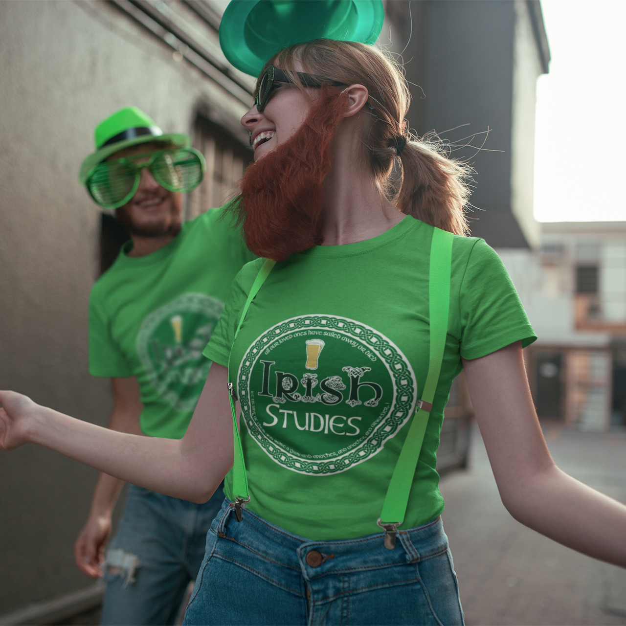 Two people wearing green shirts with 'Irish Studies' text, one person also wearing green suspenders, outdoors.