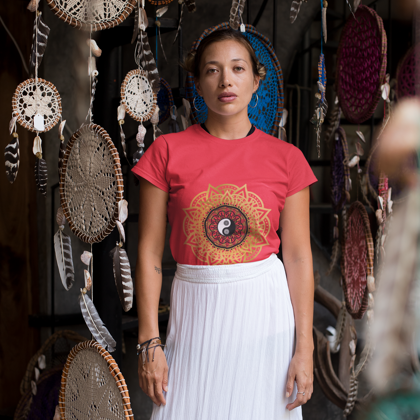 Woman wearing a red t-shirt with a colorful design in front of dreamcatchers.