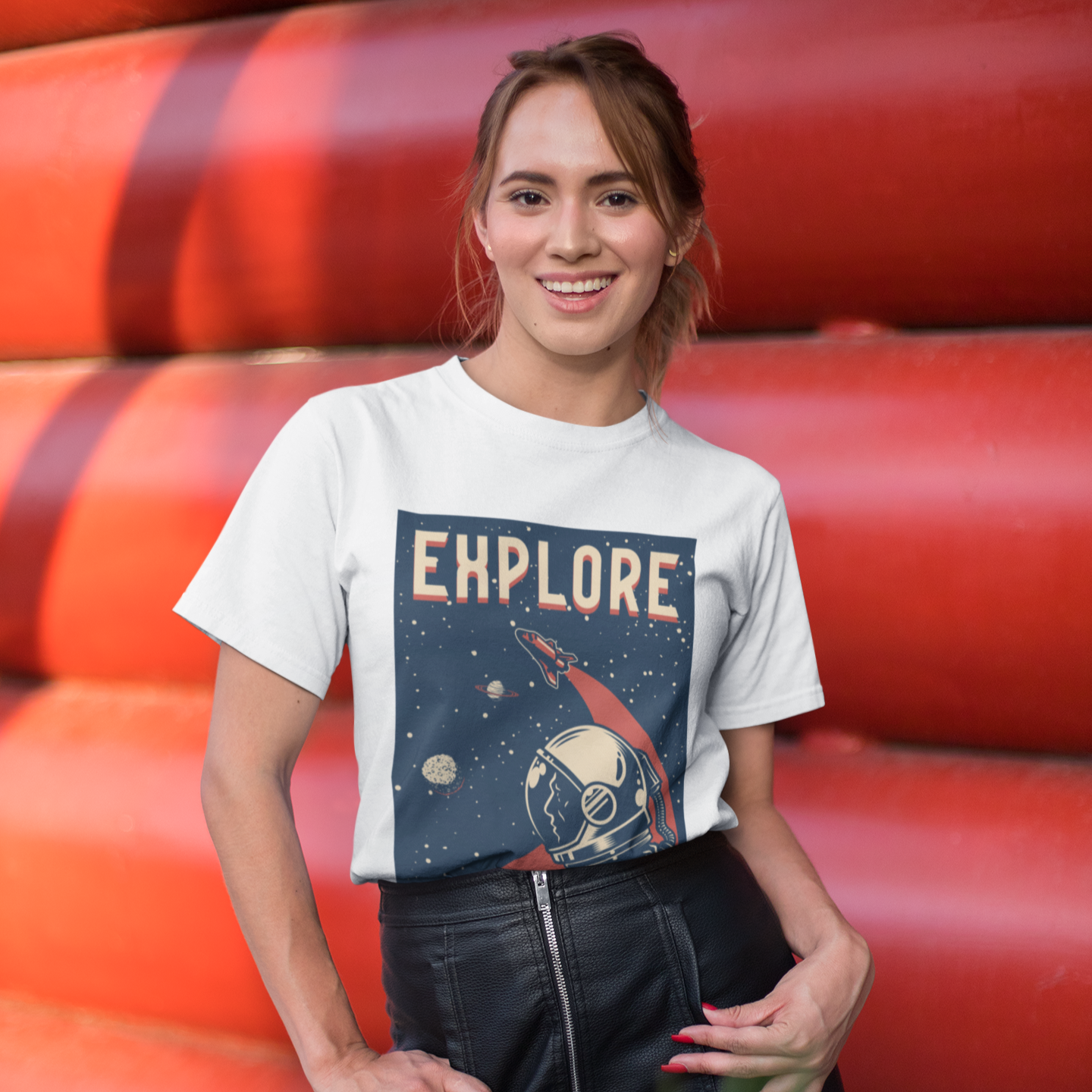 Woman wearing a white t-shirt with 'EXPLORE' printed on it, standing in front of red cylindrical objects.