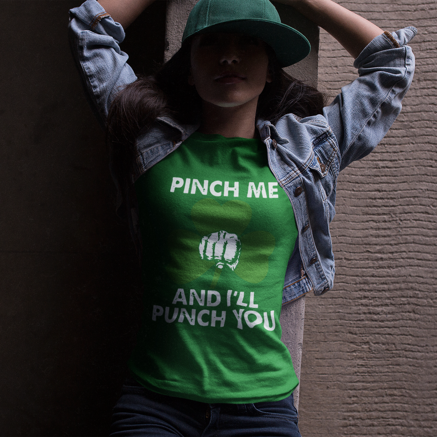 Person wearing a green t-shirt with text and a graphic, standing against a textured wall.