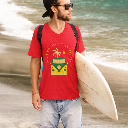 Man on a beach wearing a red t-shirt with a graphic design, holding a surfboard.