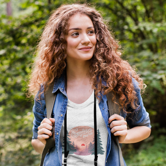 Woman with curly hair wearing a denim jacket and a graphic t-shirt in a forest setting