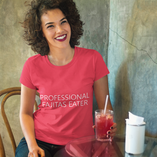 Woman wearing a pink t-shirt with 'Professional Fajitas Eater' text, sitting at a table with a drink.