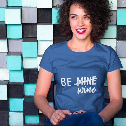 Woman wearing a blue t-shirt with 'BE MINE Wine' text against a colorful geometric wall.